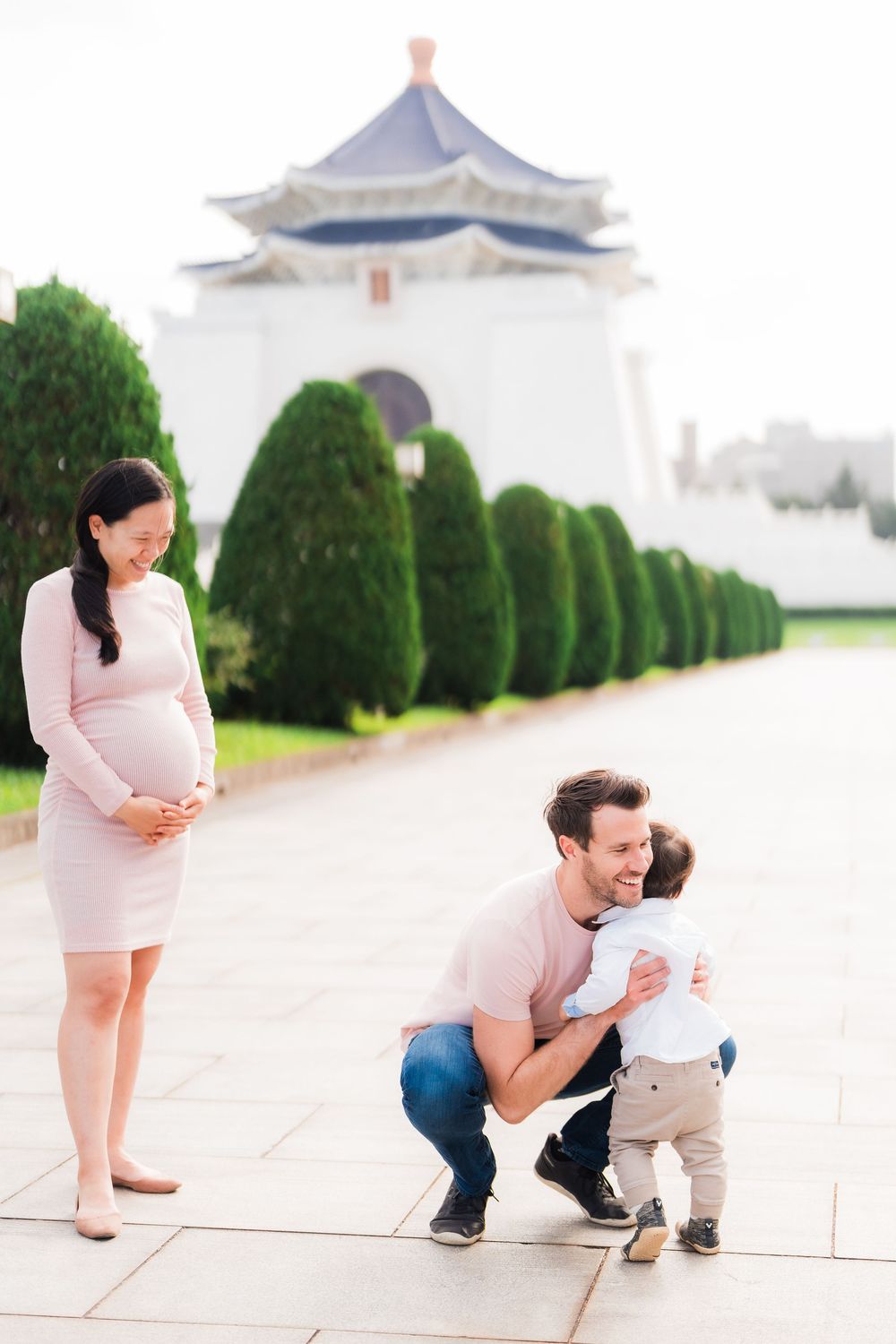 A maternity family portrait at Chiang Kai-shek Memorial Hall in Taipei with toddler and parents in pink outfits.