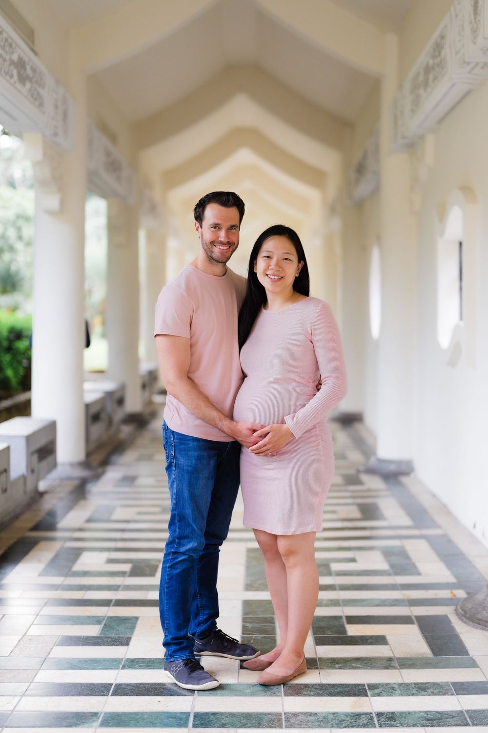 A couple wearing pink poses together in an elegant hallway with arched ceilings and patterned tile floors at CKS.