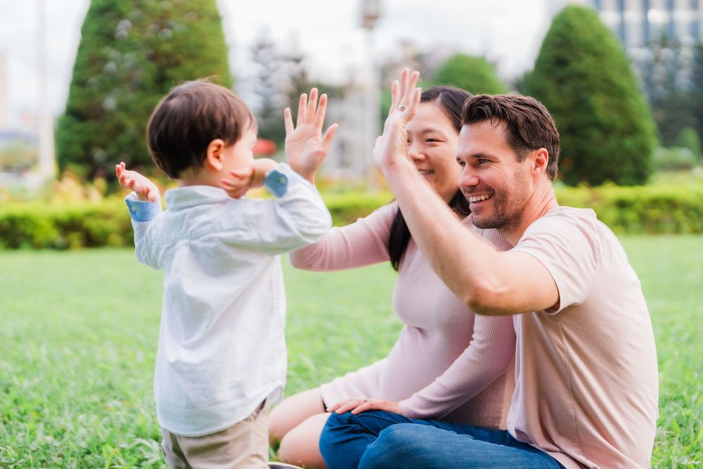 A toddler giving high fives to his parents on the grass field of CKS Memorial Hall.