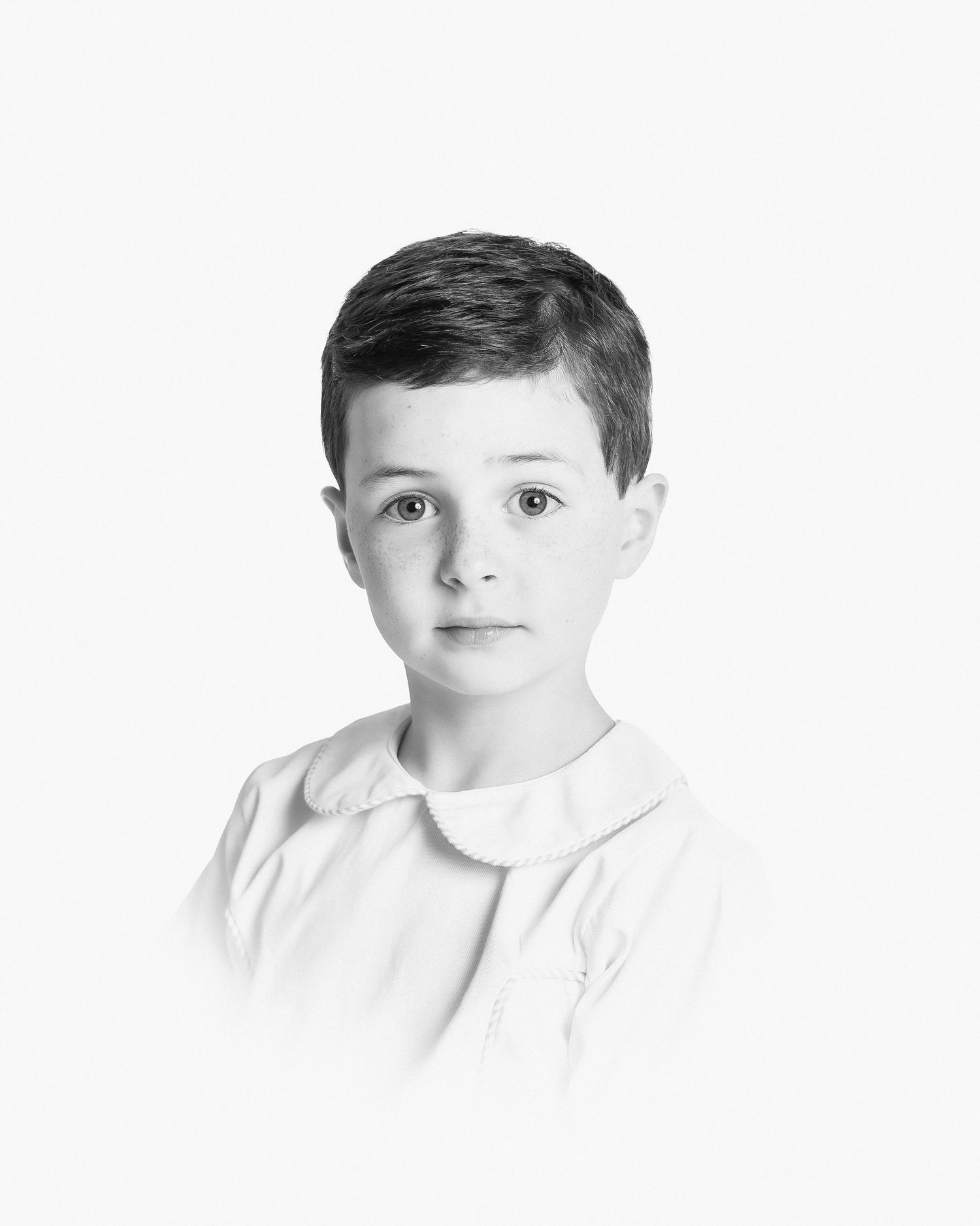 Black and white portrait of a boy wearing a white collared shirt against a plain background.
