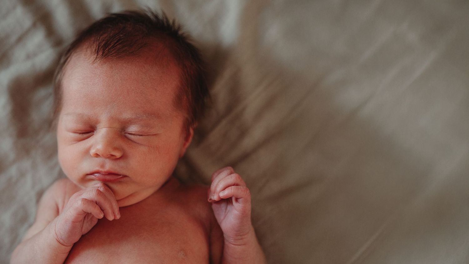Sleeping newborn baby with hand near mouth on soft beige bedding.