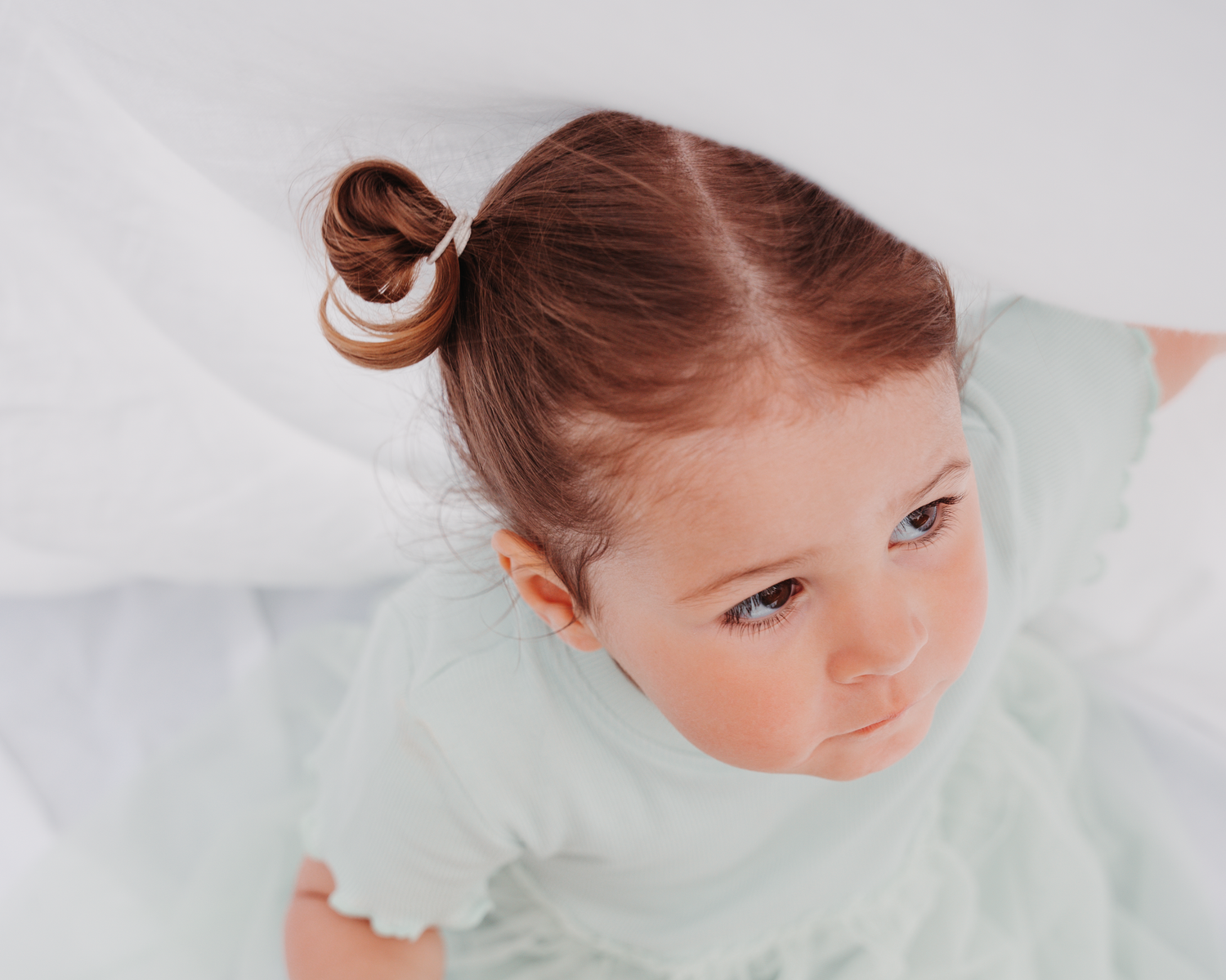 A close-up portrait showing a child with hair in a bun against a white background.