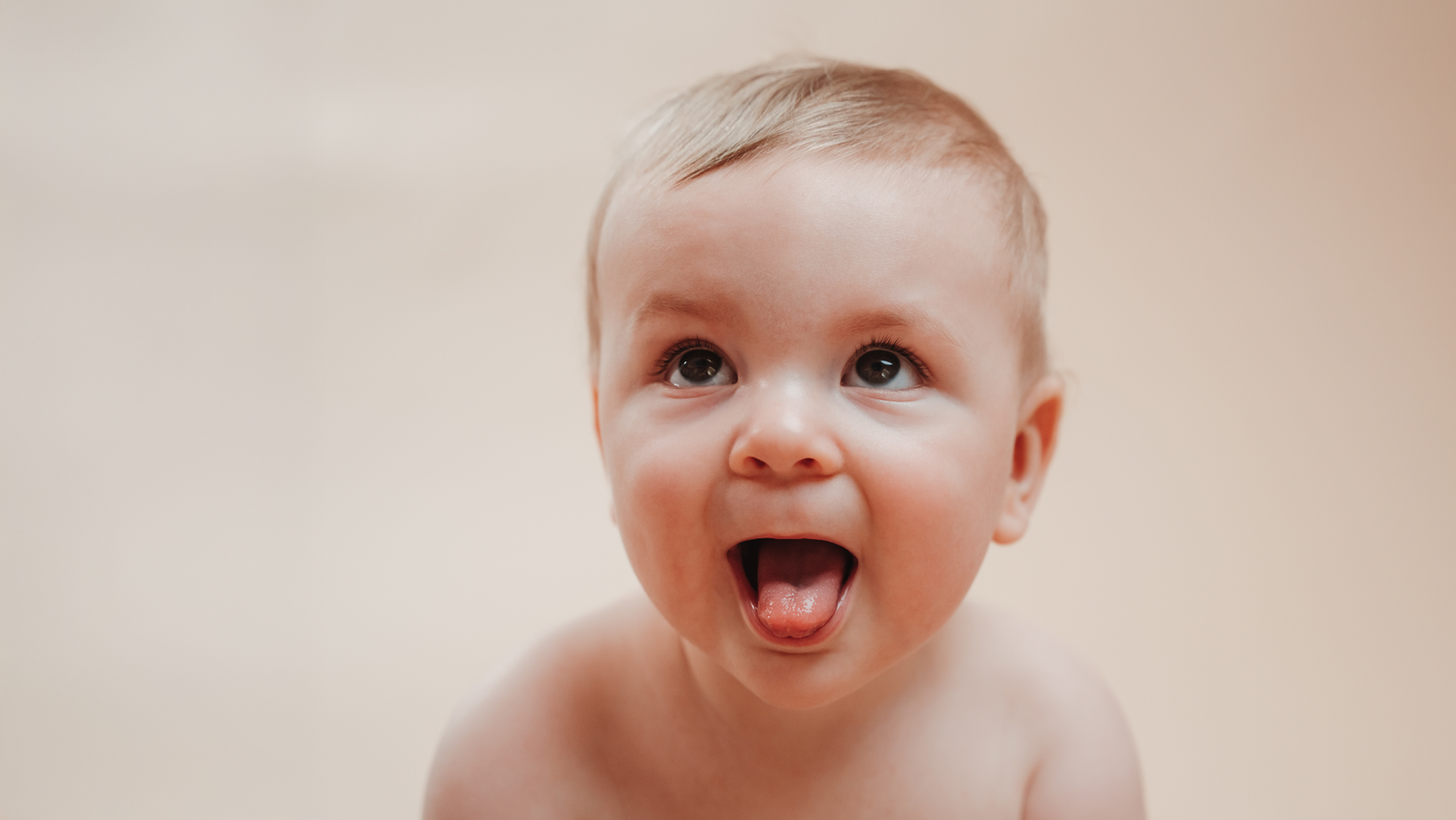 Excited baby with wide open mouth against neutral background.
