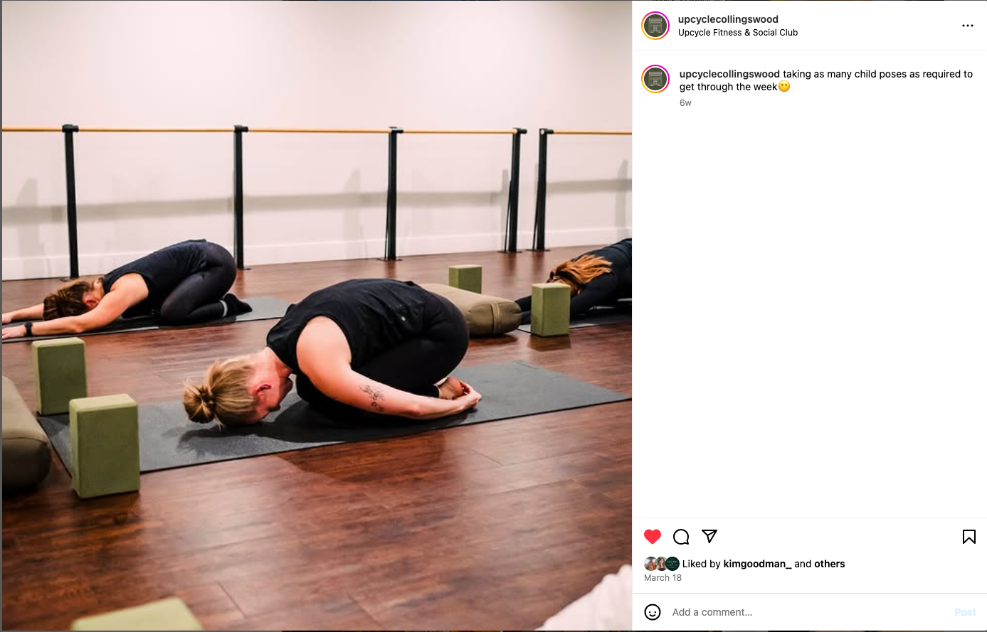 Person performing child's pose on yoga mat with green blocks in a studio with wooden floors.