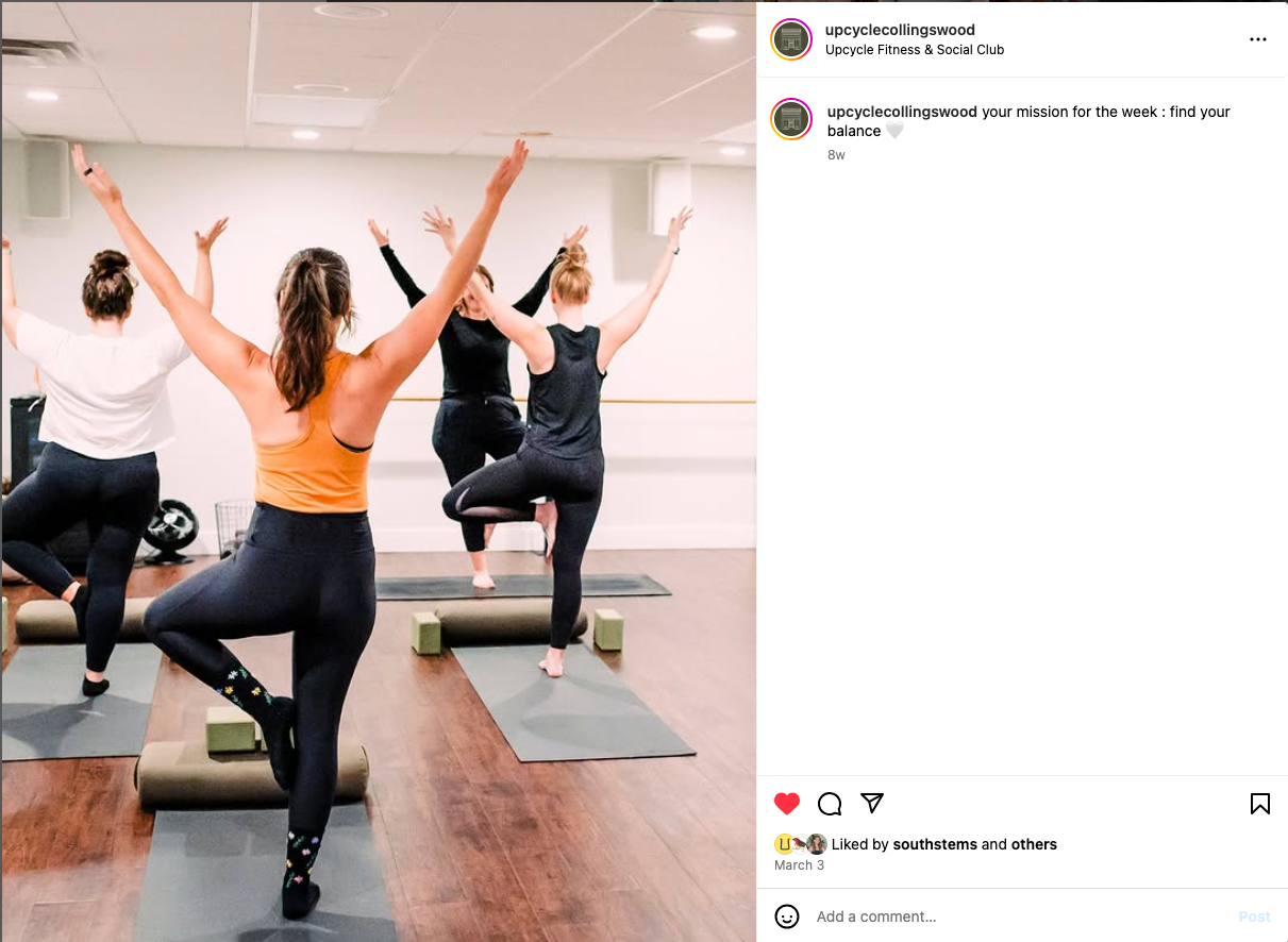 Group of students in active workout wear doing a standing yoga pose in a bright studio space.