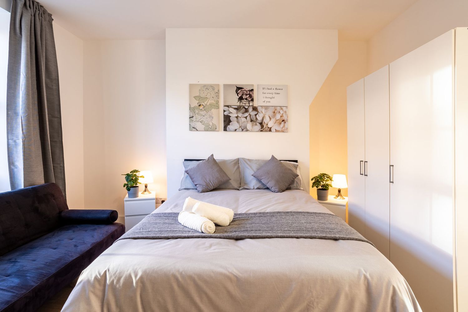Modern bedroom interior with gray bedding, navy couch, white walls and artwork featuring decorative yellow accents.