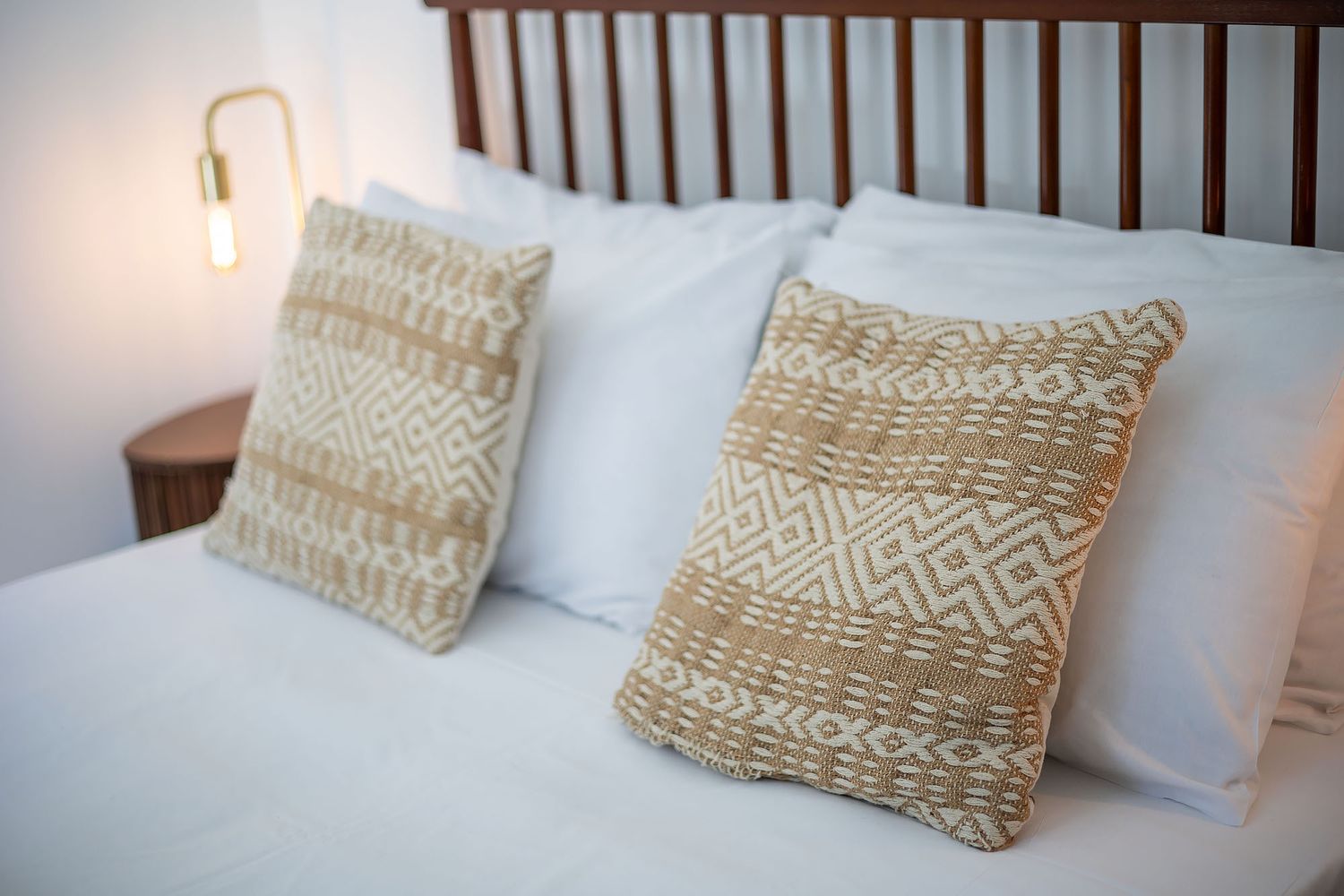 Close-up of a bed with crisp white linens and textured beige geometric pattern throw pillows.