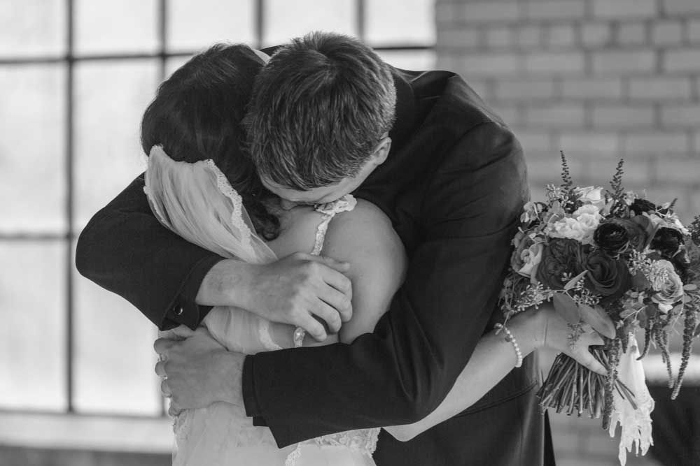 A romantic black and white wedding photo capturing a loving embrace with a bouquet of flowers.