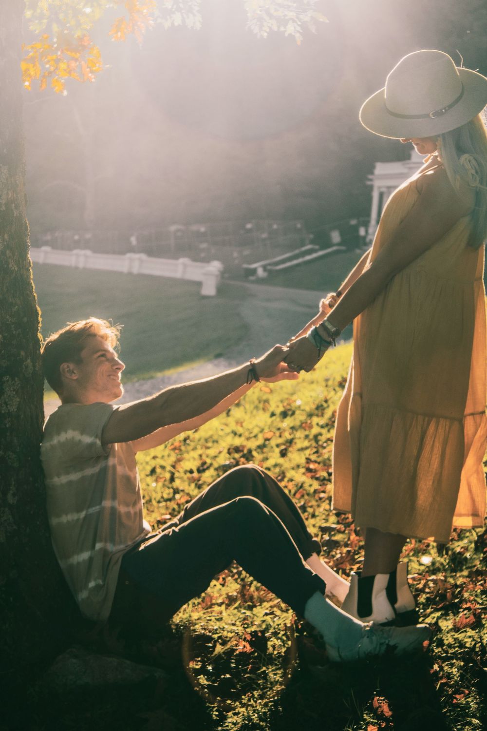 man sitting against tree with woman standing while holding hands