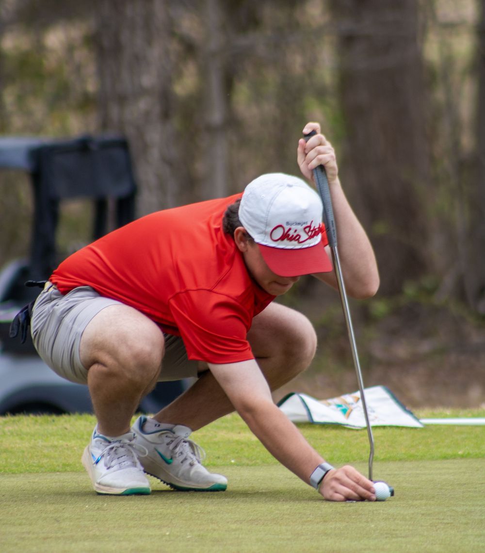 golfer lining up shot on putting green in red shirt