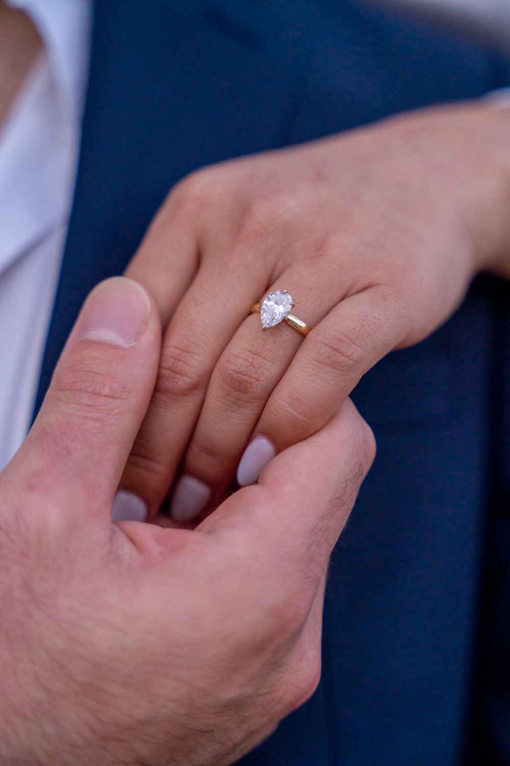 Close-up of hands with engagement ring being placed on finger showing classic solitaire diamond ring.