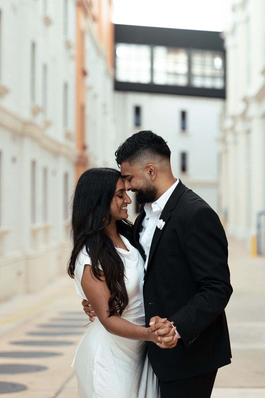 Intimate wedding couple sharing a romantic dance in formal attire against an urban backdrop.