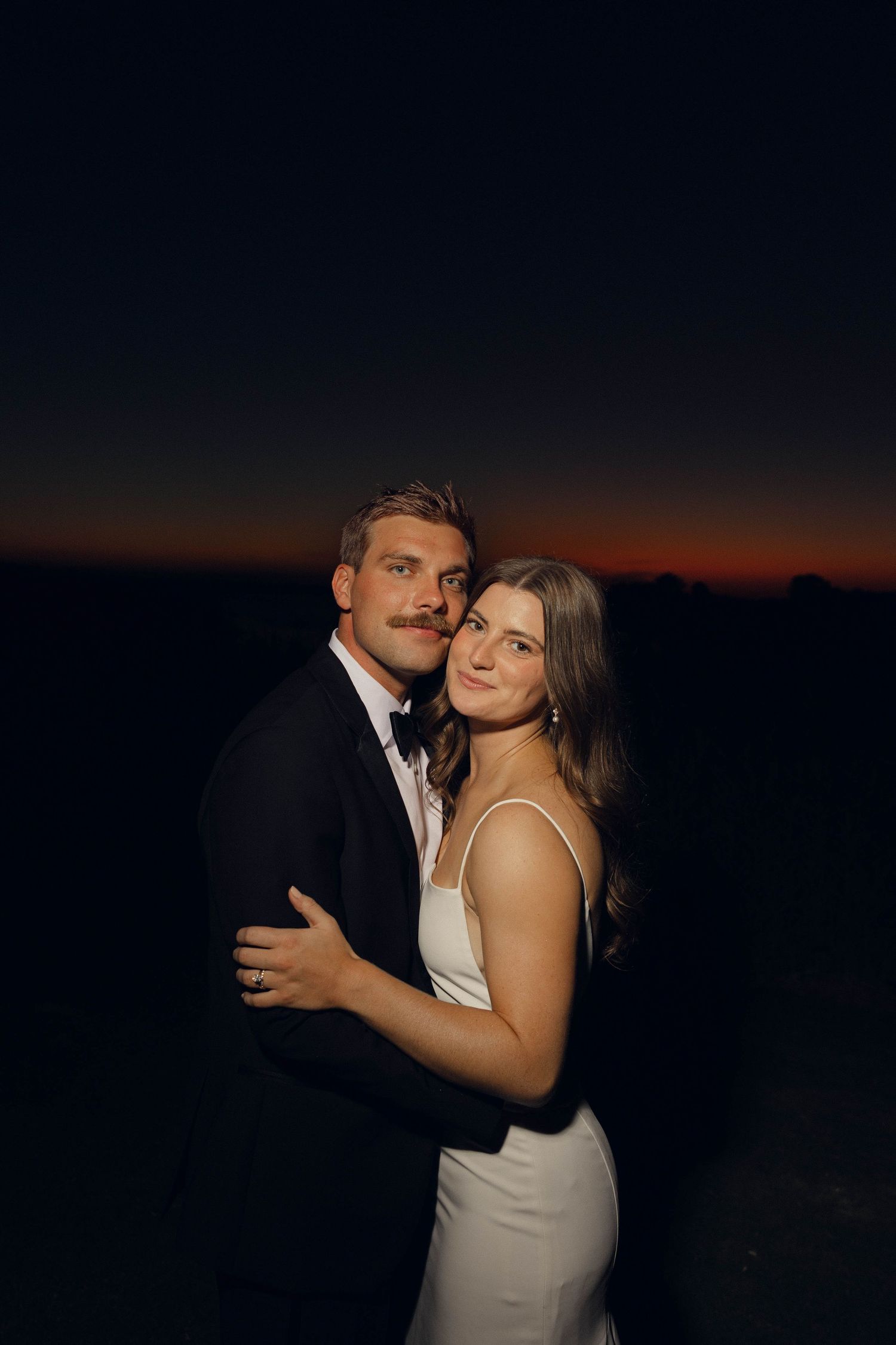 Wedding couple posing separately on beach with bride holding bouquet and groom in foreground.