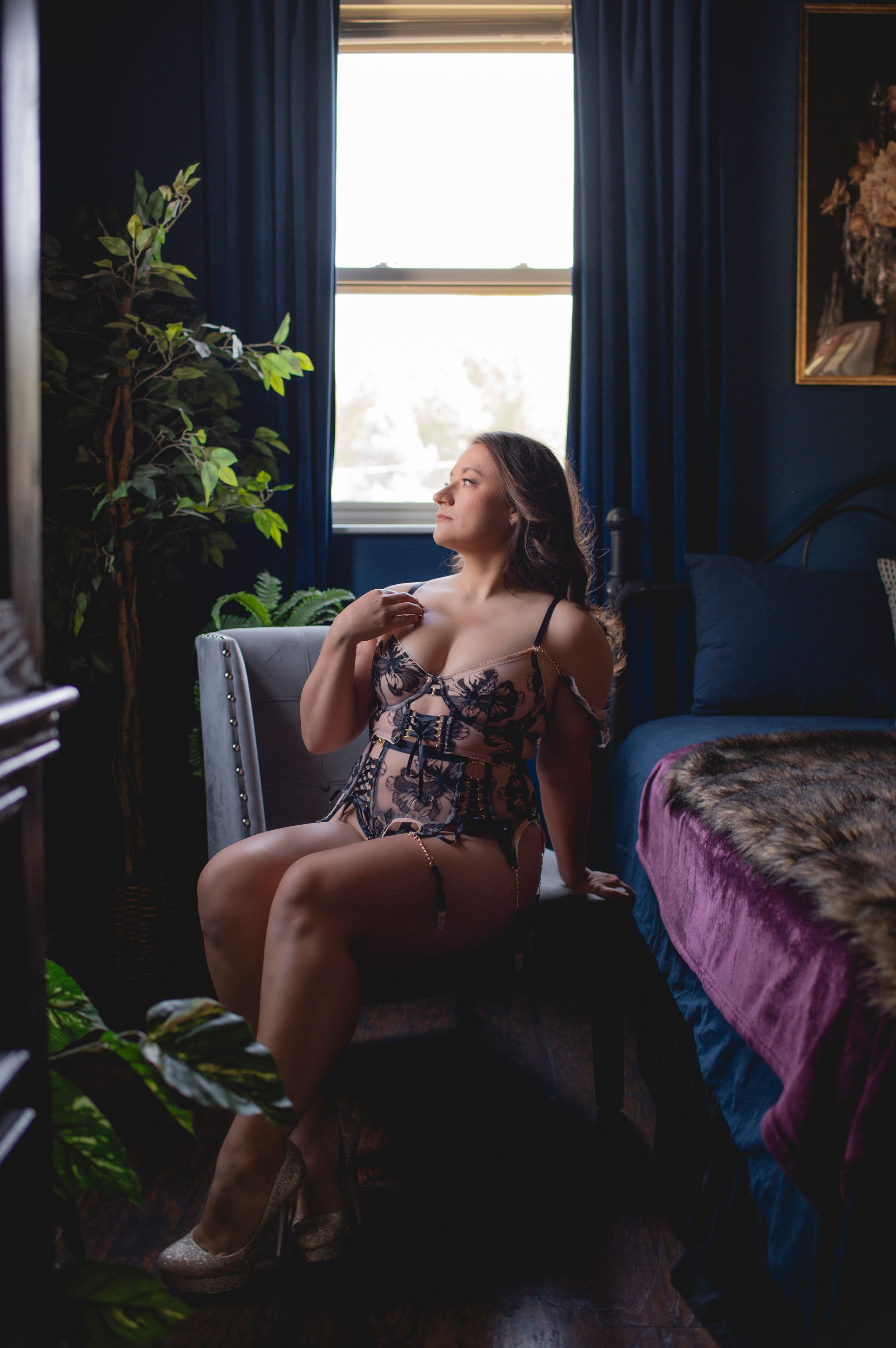 A series of artistic boudoir photos showing a figure by a window with dark blue curtains and natural lighting.