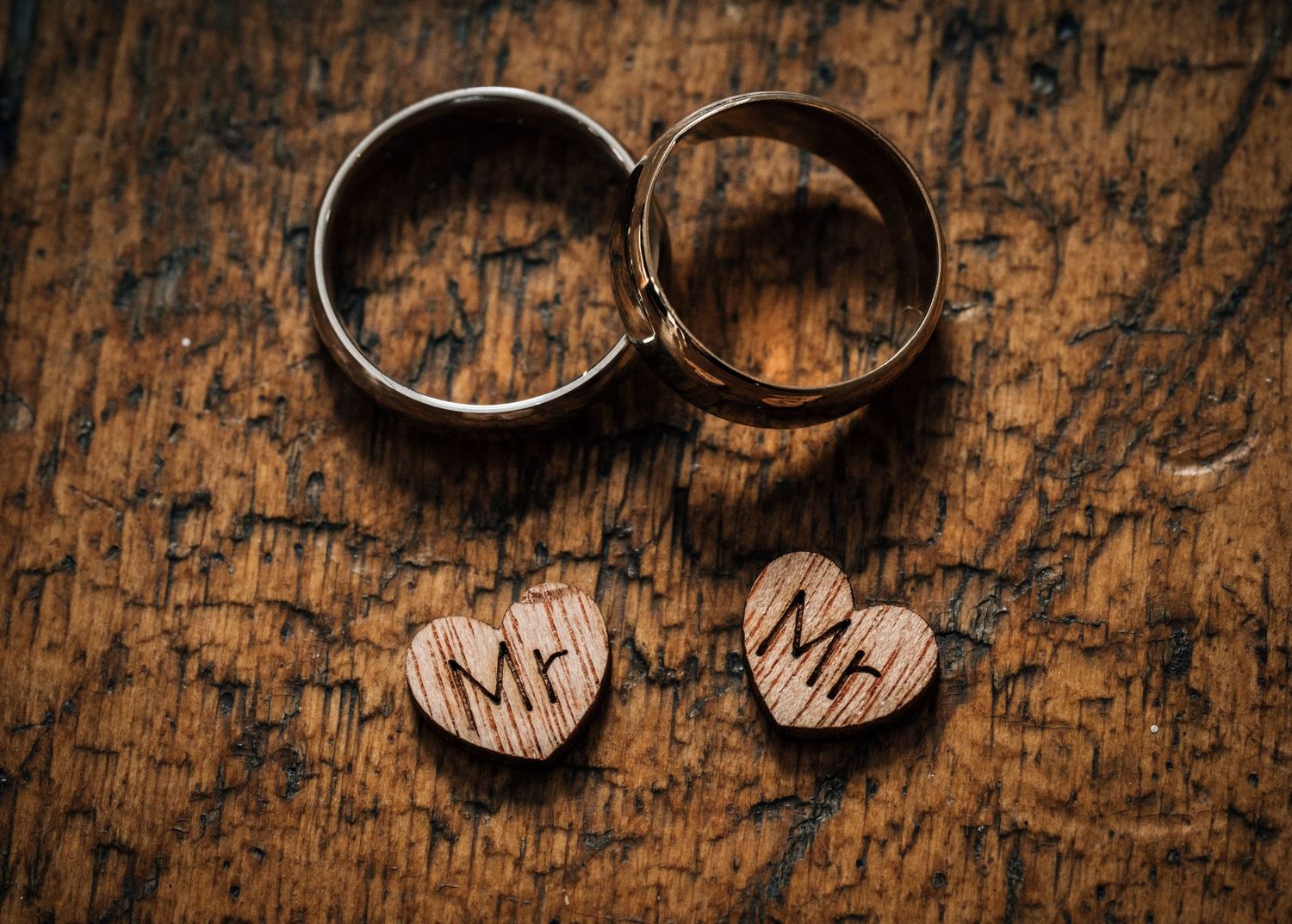 Two wedding rings and wooden hearts with Mr and Mrs text on rustic wooden background.