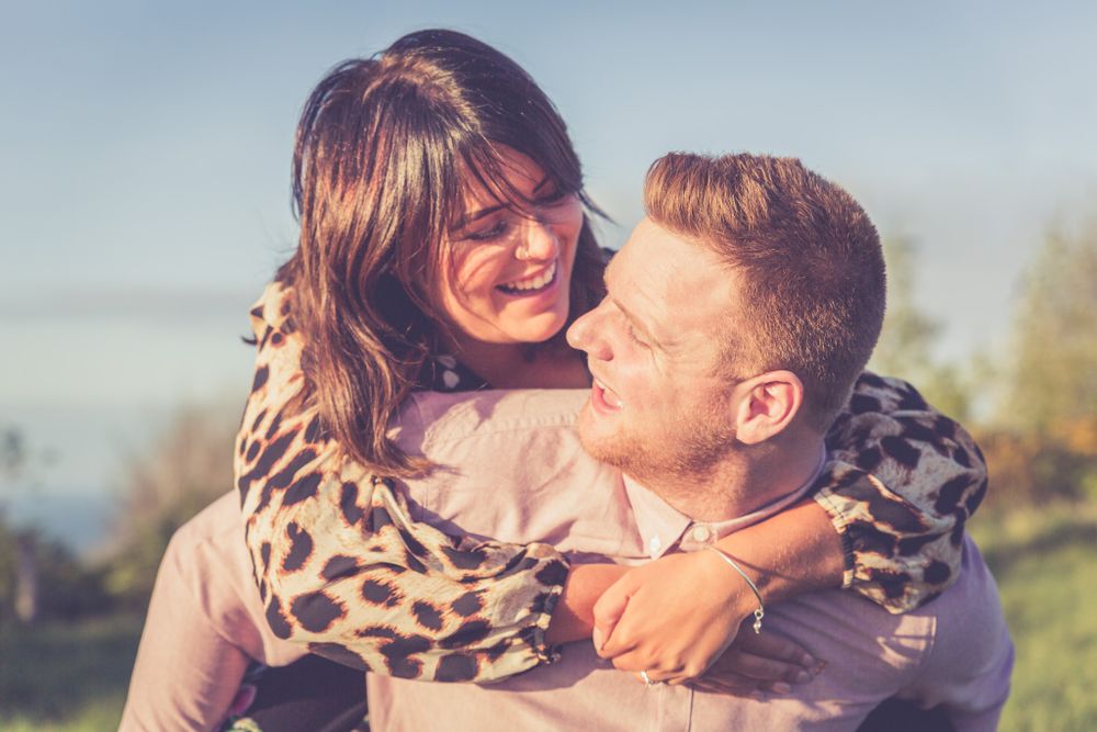 A portrait of a loving couple. The lady throws her arms around her partner from behind. North Wales Couple Photographer