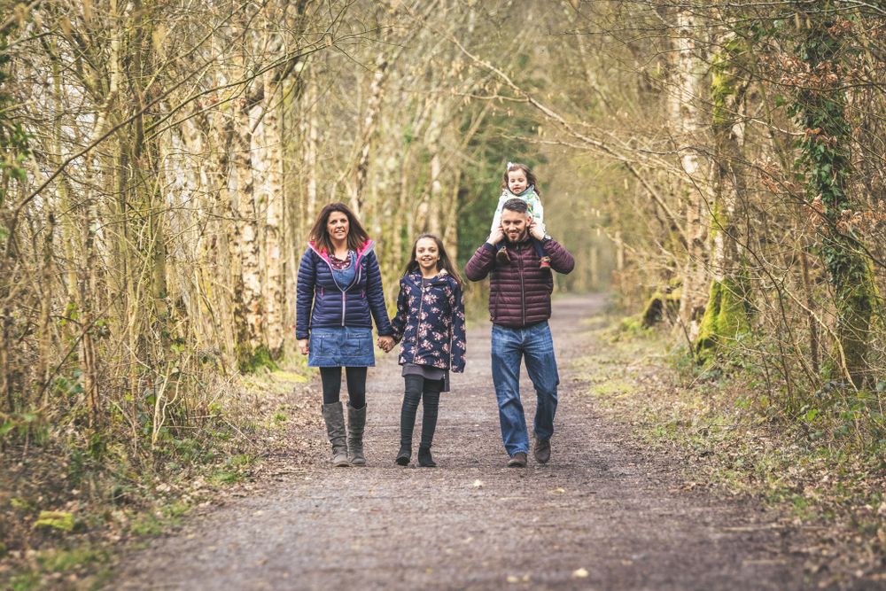A family, Mum, Dad and 2 girls, one on Dad's shoulders, are walking down a woodland path near Dolgellau. Gwynedd Portrait Photographer