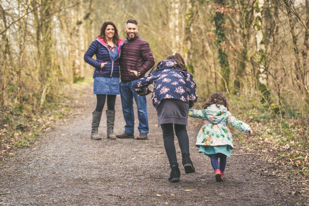 A family portrait. 2 young girls running towards Mum and Dad on a woodland path near Dolgellau. North Wales Portrait Photography