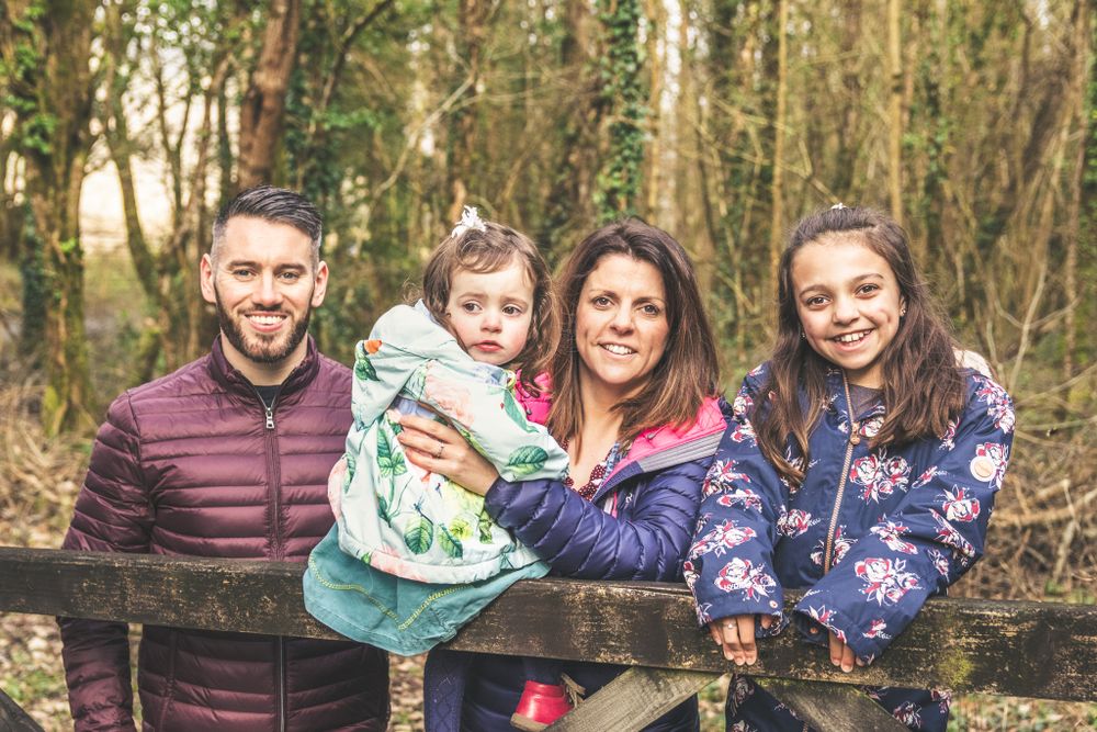 A portrait of a family of 4 posing on a gate at the side of a woodland path. North Wales Family Portrait Photographer