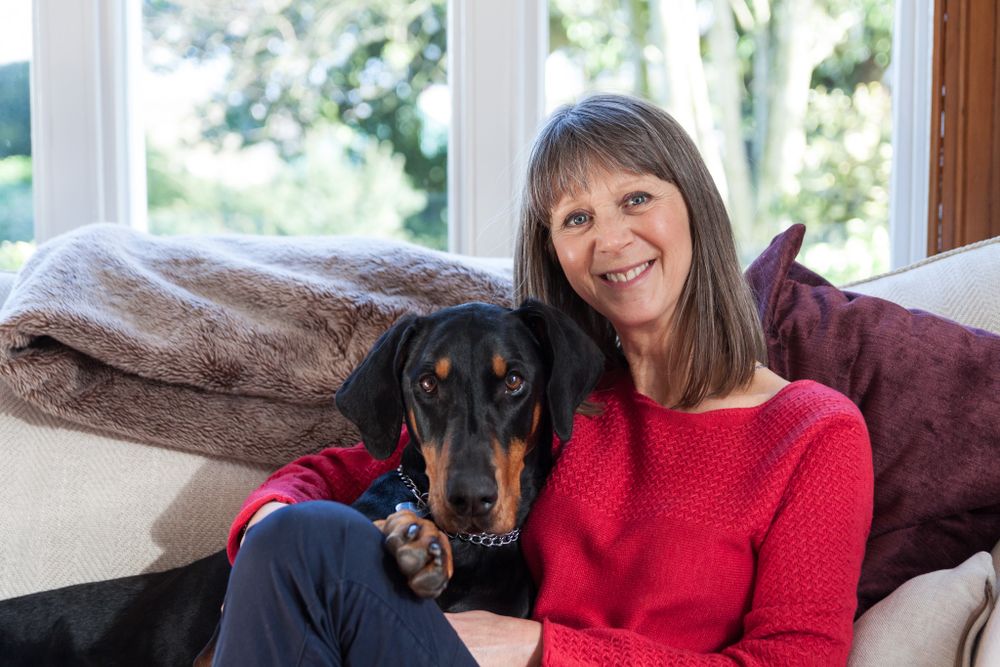 A portrait of a lady in a red jumper cuddling up on the sofa with her Doberman. North Wales Portrait Photographer