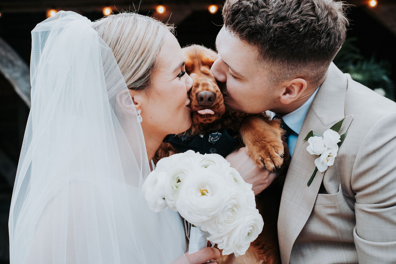 Couple shares joyful moment with their small dog during wedding ceremony while holding white peony bouquet.