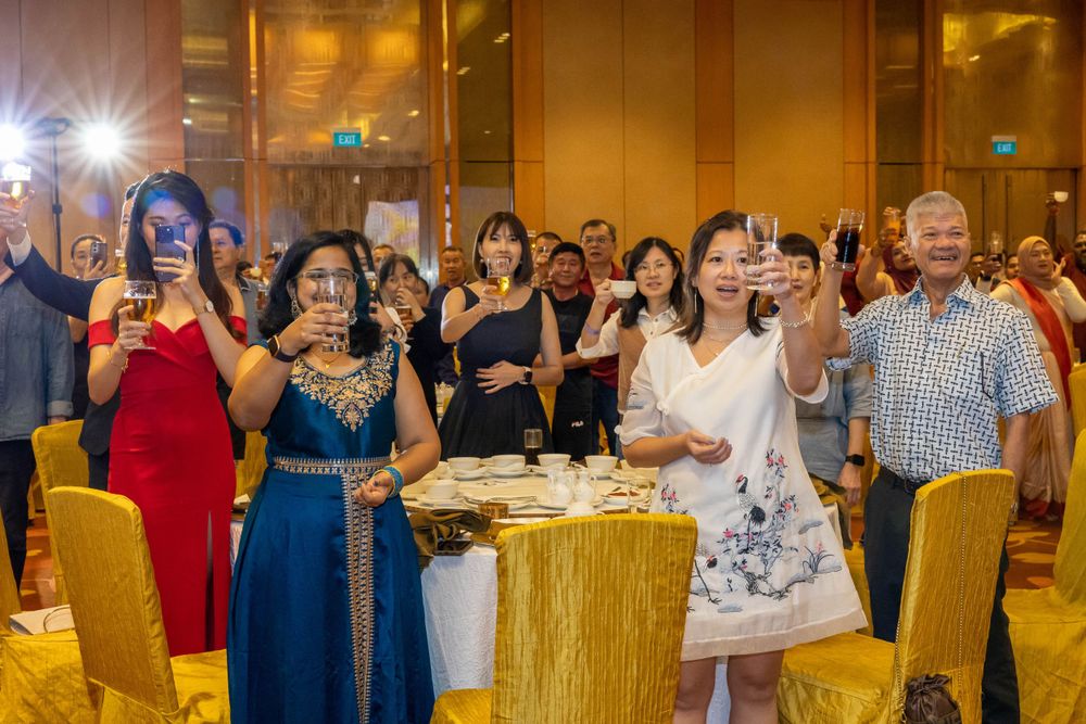Event attendees in formal attire raise their phones with flashlights at an elegant venue with gold chairs.