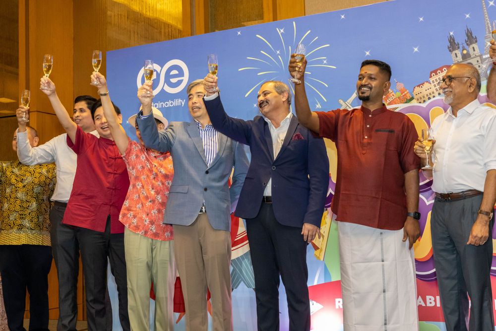 People raising their hands in celebration on stage against a bright blue backdrop with festive decorations.