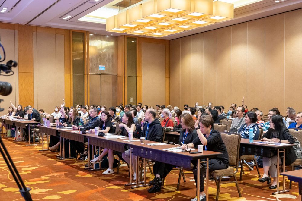 Large corporate conference room filled with attendees seated at long tables during presentation.
