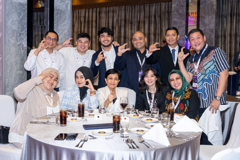 Business professionals gather around a formal dining table for a group photo at an event.