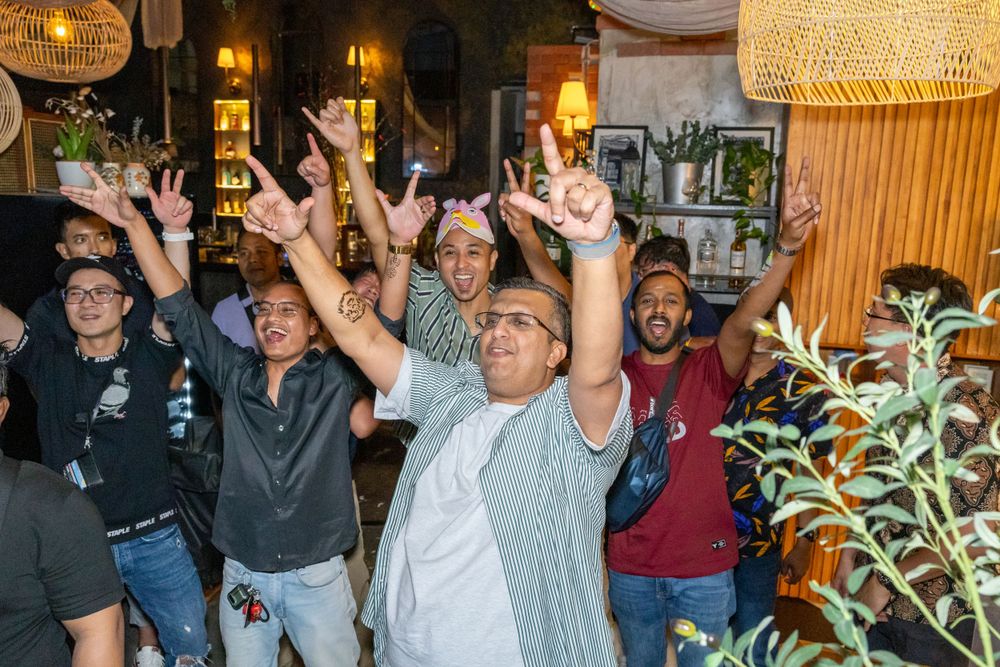 A crowd of enthusiastic people with raised arms celebrating in a warmly lit indoor venue.