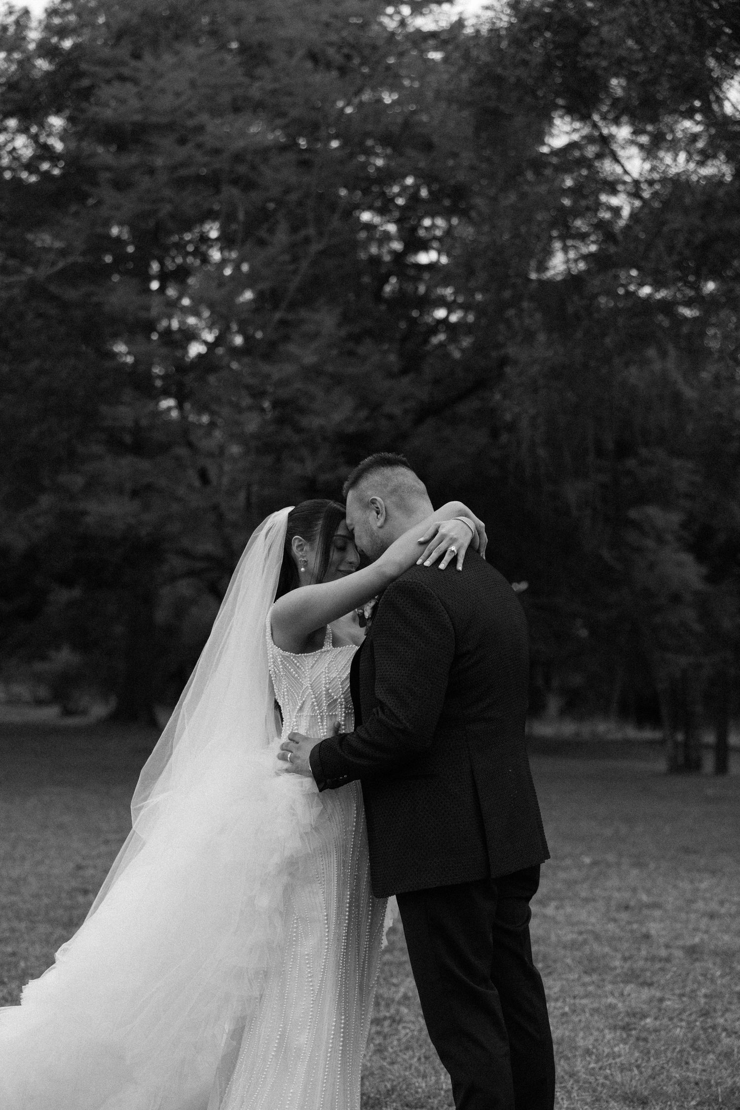 An intimate black and white wedding portrait captured in a tranquil outdoor garden setting.