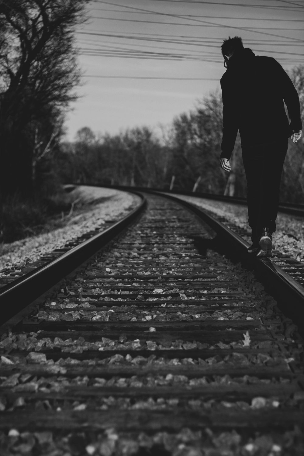 Silhouette walking on curved train tracks through wooded area in black and white.