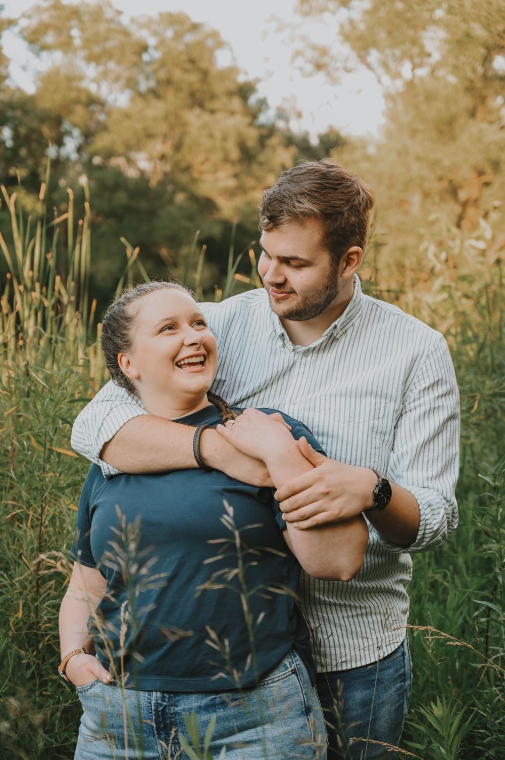 A happy couple embraces in a field of tall grass during golden hour sunset.