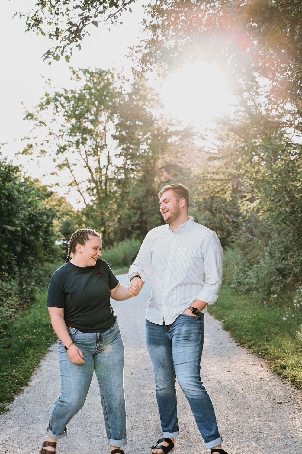 Two people holding hands while walking together on a peaceful sunlit nature trail surrounded by greenery.