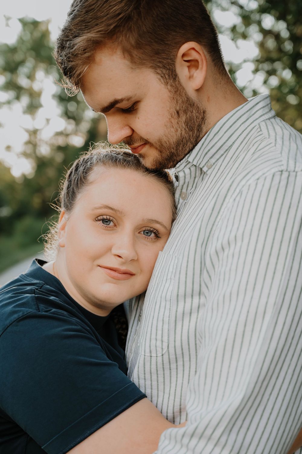 A couple shares an intimate close-up moment outdoors against a natural background.