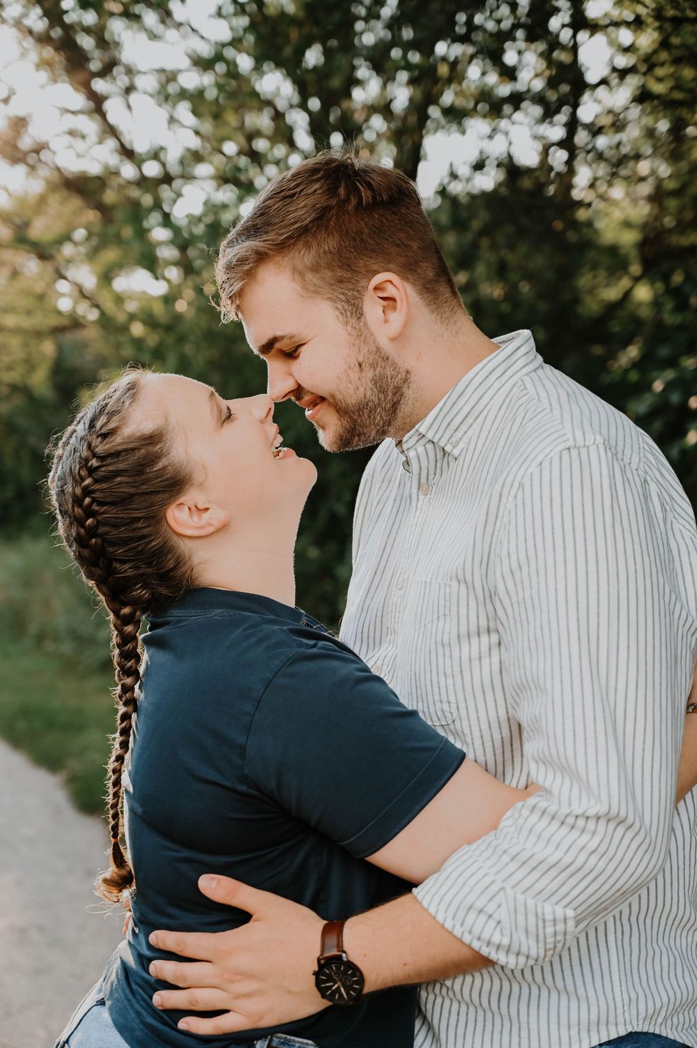 A romantic outdoor portrait of a couple embracing and sharing an intimate moment in dappled sunlight.
