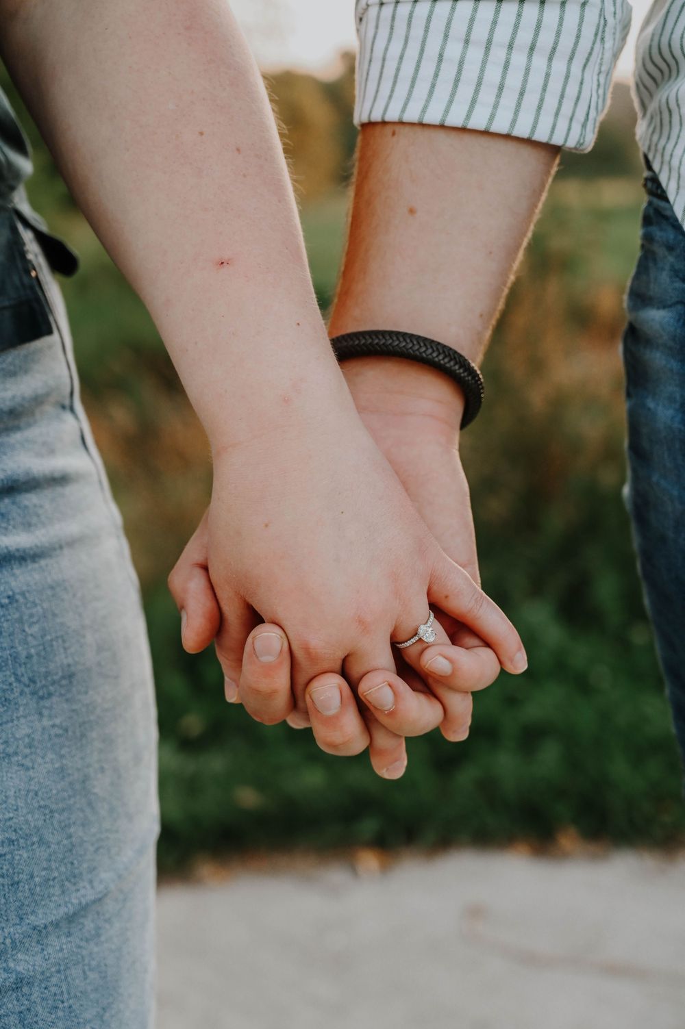 Close-up shot of two people holding hands while wearing casual clothing and denim jeans outdoors.