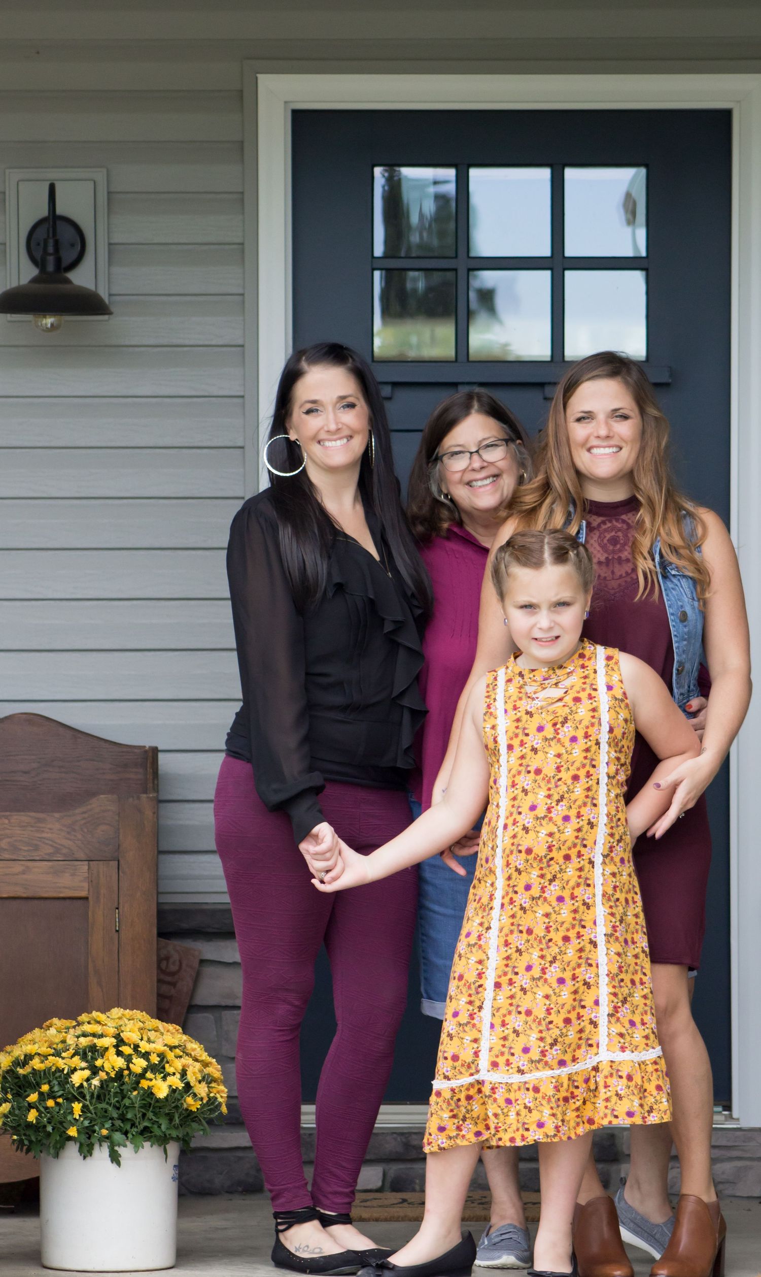 Three women and a young girl posing on a home front porch in autumn.