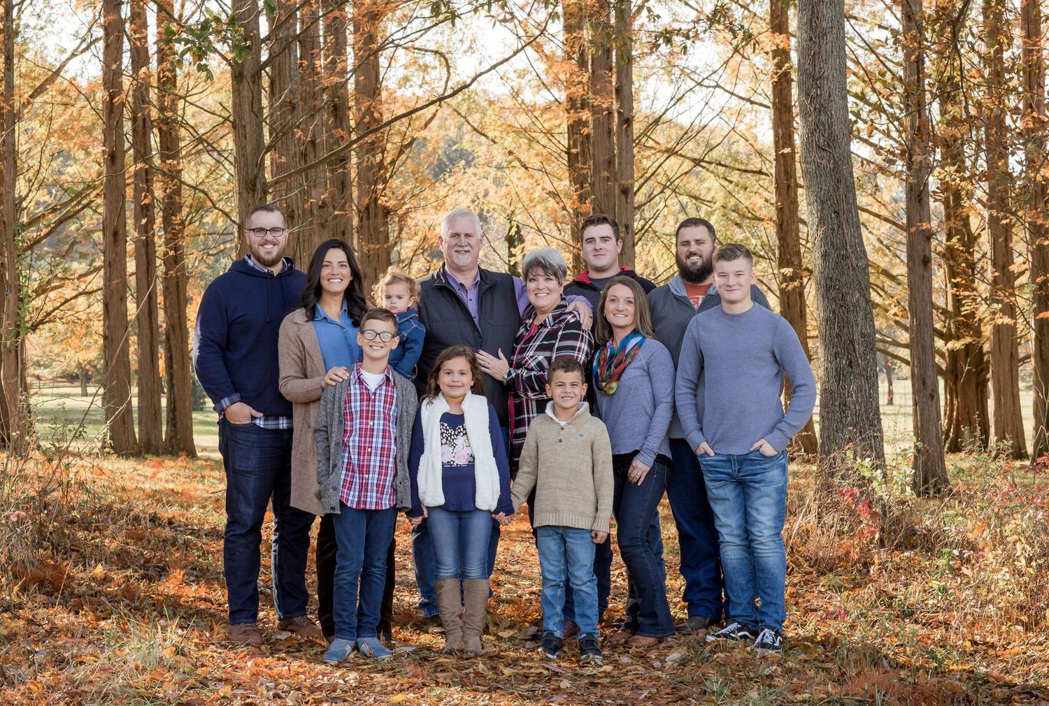 A large multigenerational family poses together among colorful autumn trees in a fall outdoor portrait.