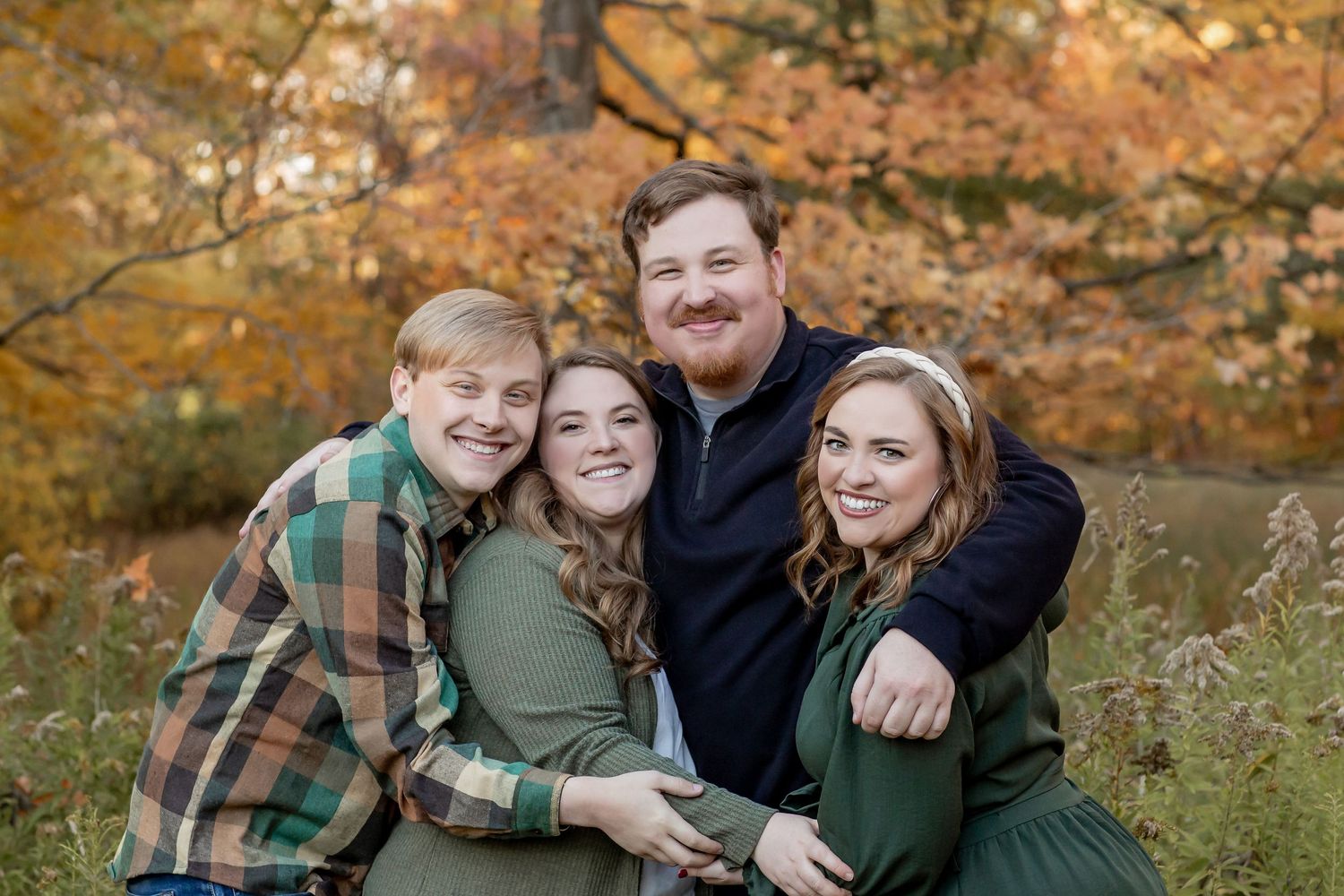 Happy family of four embracing outdoors with colorful autumn foliage background.