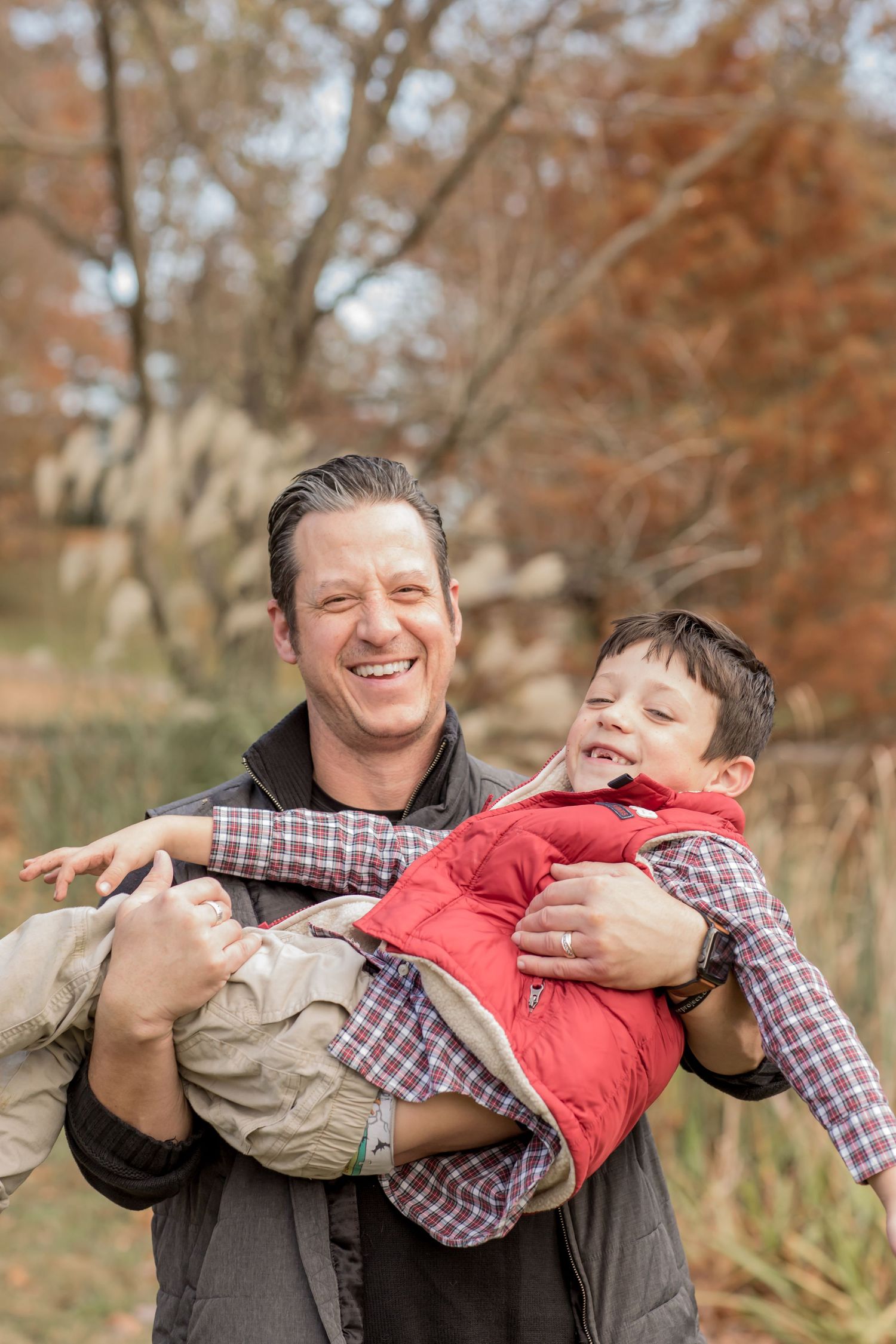 Smiling father holding his laughing young son outdoors during autumn season.