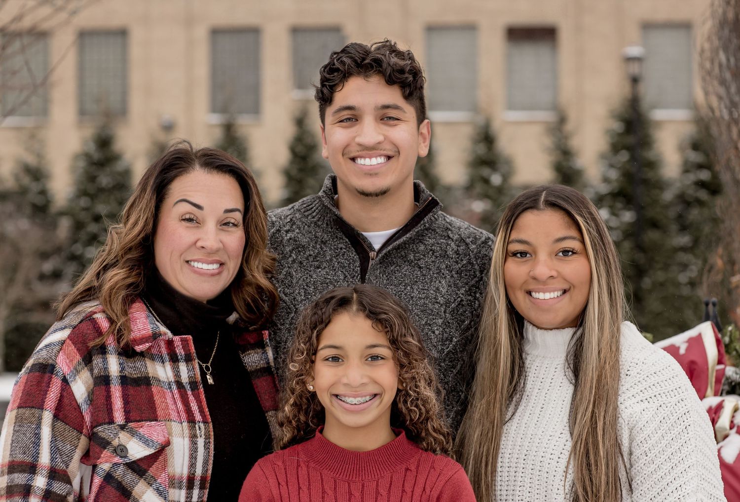 Family of four smiling together outdoors in front of a building in winter.