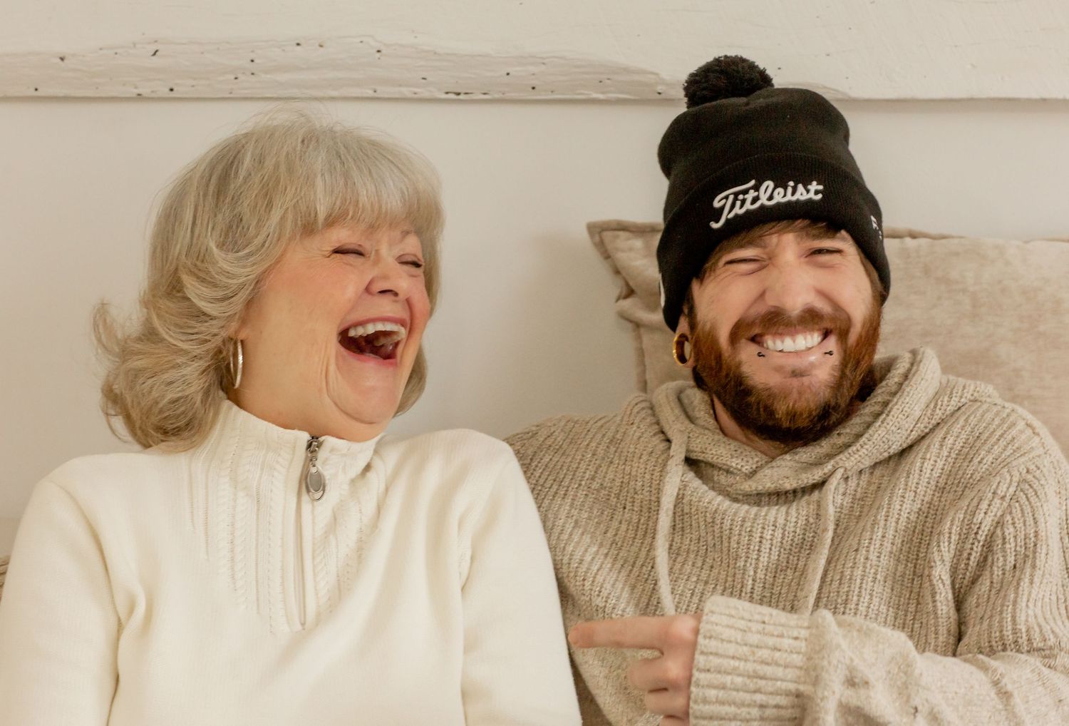 Laughing mother and son sharing a joyful moment together indoors, son wearing a Titleist beanie.