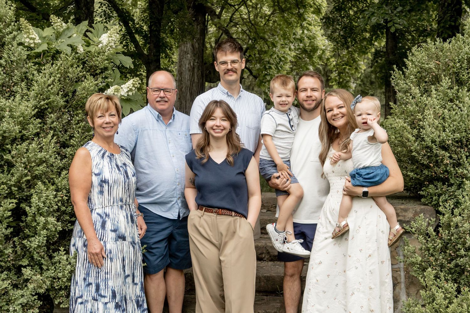 Happy multigenerational family of seven posing together outdoors among lush green foliage.