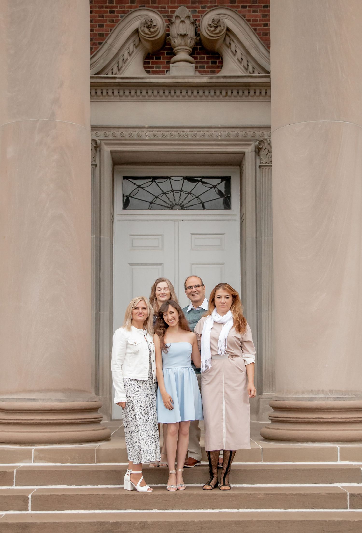 Family of five posing on steps of elegant building with ornate white door.