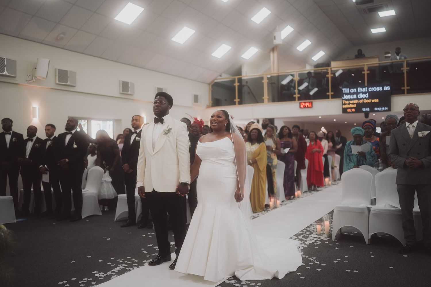 Wedding celebration in church hall with guests and couple walking down aisle.