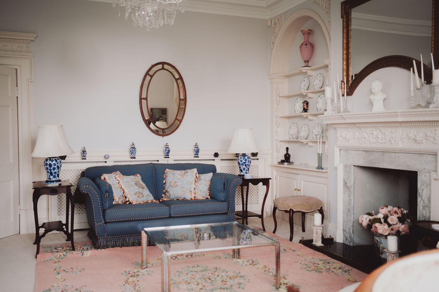 Elegant living room with blue sofa, ornate mirror, and white fireplace mantel.