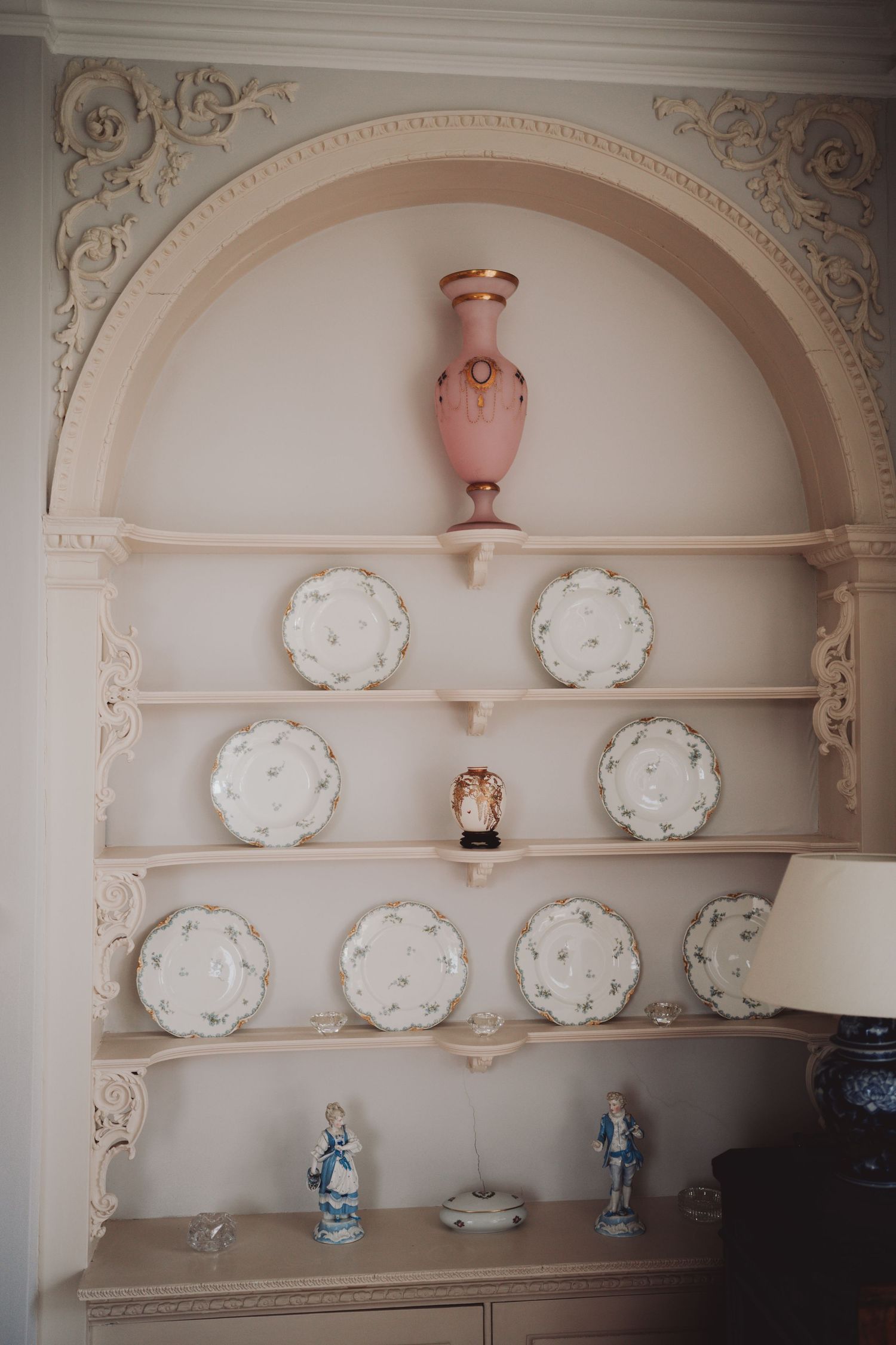 Ornate wall alcove displaying white decorative plates and ceramic vases with intricate molding details.