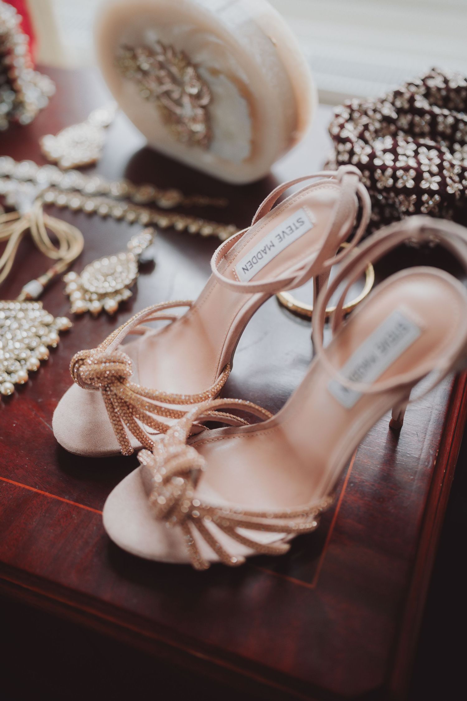 Blush pink strappy wedding heels with metallic accents on a wooden surface.