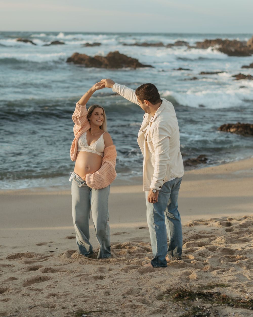 Romantic couple shares intimate moments while walking along a rocky beach at sunset.